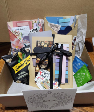 various items, including a card, a ribbon, and some snacks, all placed in a cardboard box.