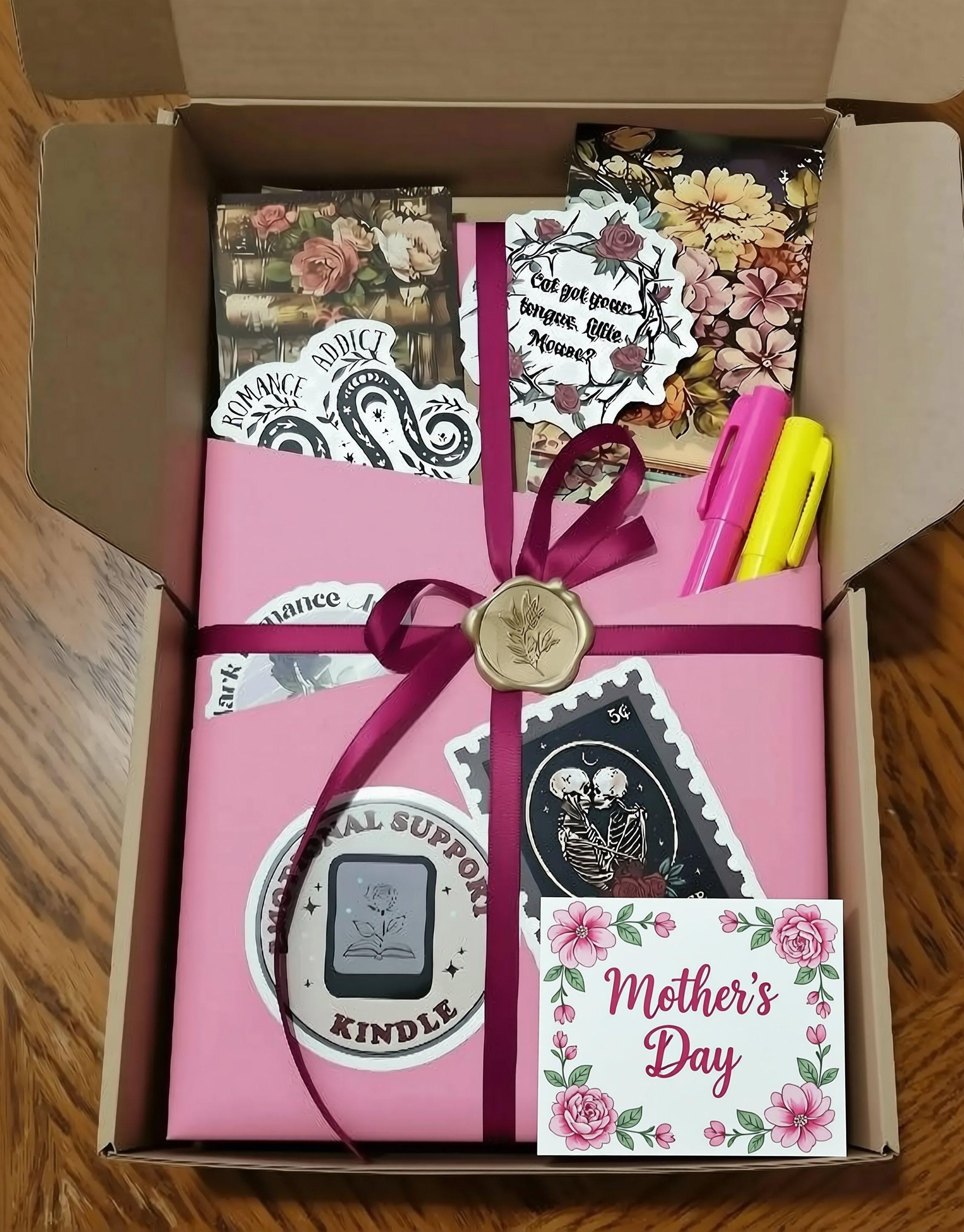 A pink box containing various items, including a book, a stamp, and some other decorative elements, all tied together with a purple ribbon.