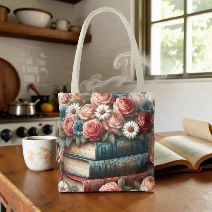 A tote bag with a floral design featuring a stack of books with roses and daisies on top.