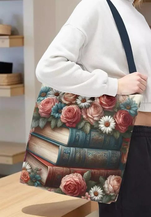 A tote bag with a floral design featuring a stack of books with roses and daisies on top.