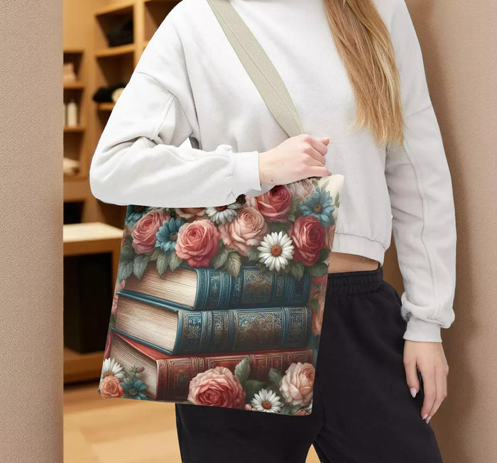 A tote bag with a floral design featuring a stack of books with roses and daisies on top.