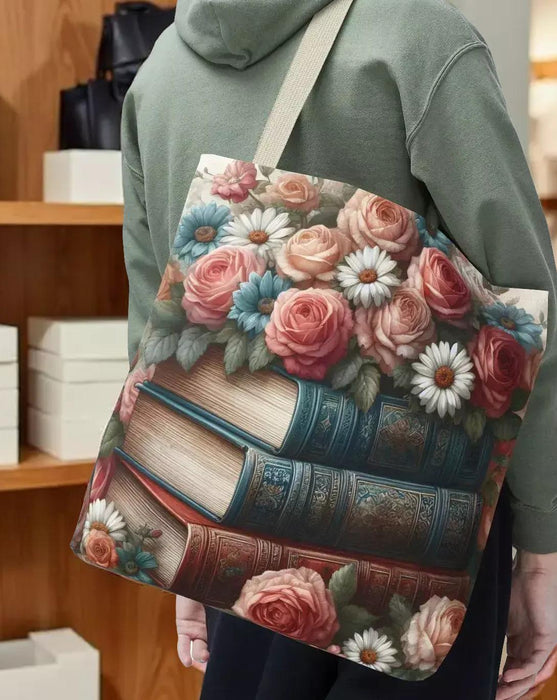A tote bag with a floral design featuring a stack of books with roses and daisies on top.