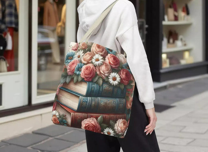 A tote bag with a floral design featuring a stack of books with roses and daisies on top.