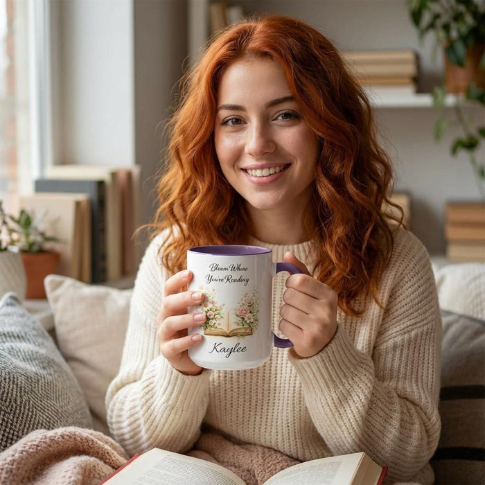 A white mug with a blue handle, featuring an illustration of an open book surrounded by flowers.