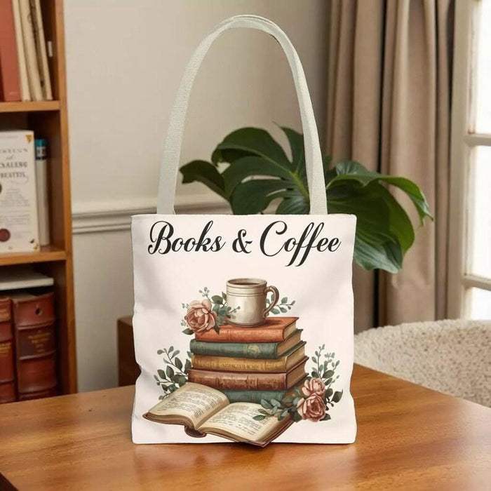 A white tote bag with a printed design of a stack of books and a cup of coffee, placed on a wooden table in a living room setting.