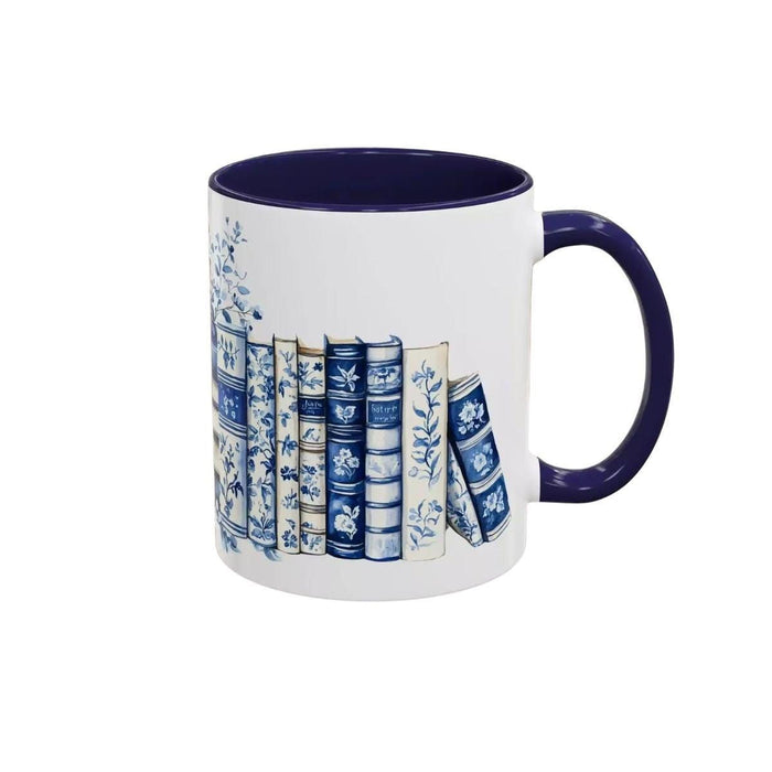 A white tote bag with a blue floral design and a stack of blue and white books, along with a matching blue and white mug, are displayed on a wooden surface.