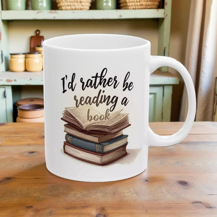 A beige tote bag with a printed design on it, depicting a stack of books. The text on the bag reads "I'd rather be reading a book".