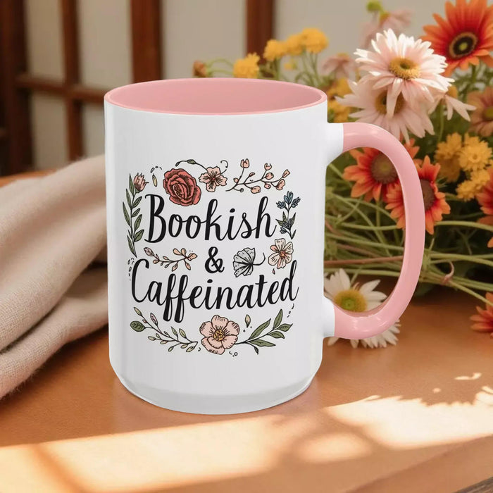 A white tote bag with a floral design and a purple handle, along with a white mug with a floral design and a purple handle, both sitting on a beige surface.