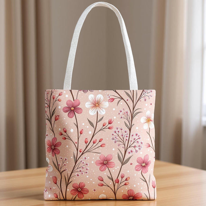 A tote bag with a floral pattern and a travel mug are displayed on a table, along with a book and some rose petals.
