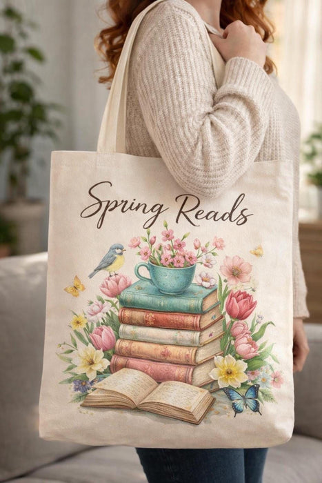 A beige tote bag with a floral design and a stack of colorful books.