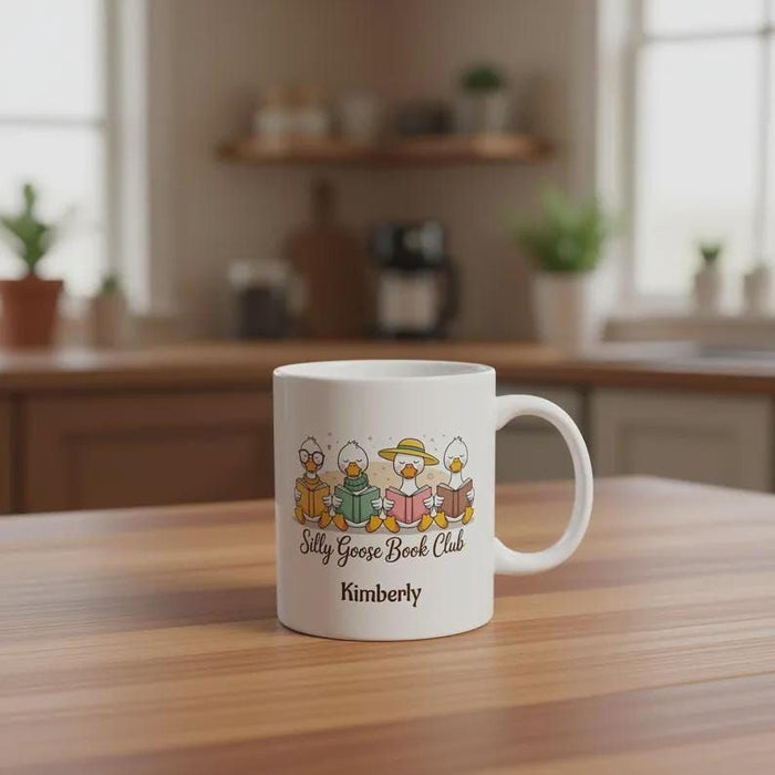 A tote bag and a travel mug with a design featuring cartoon ducks and the text "Silly Goose Book Club" are displayed on a wooden table.