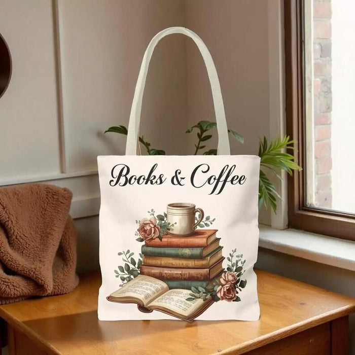 A white tote bag with a printed design of a stack of books and a cup of coffee, placed on a wooden table in a living room setting.