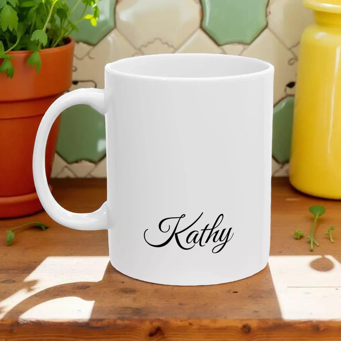 A white tote bag with a printed design of a stack of books and a cup of coffee, placed on a wooden table in a living room setting.