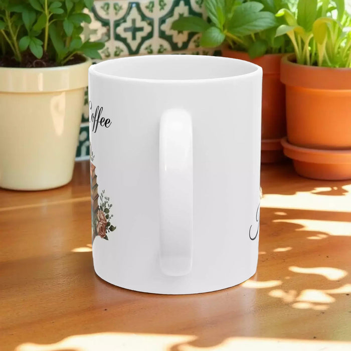 A white tote bag with a printed design of a stack of books and a cup of coffee, placed on a wooden table in a living room setting.