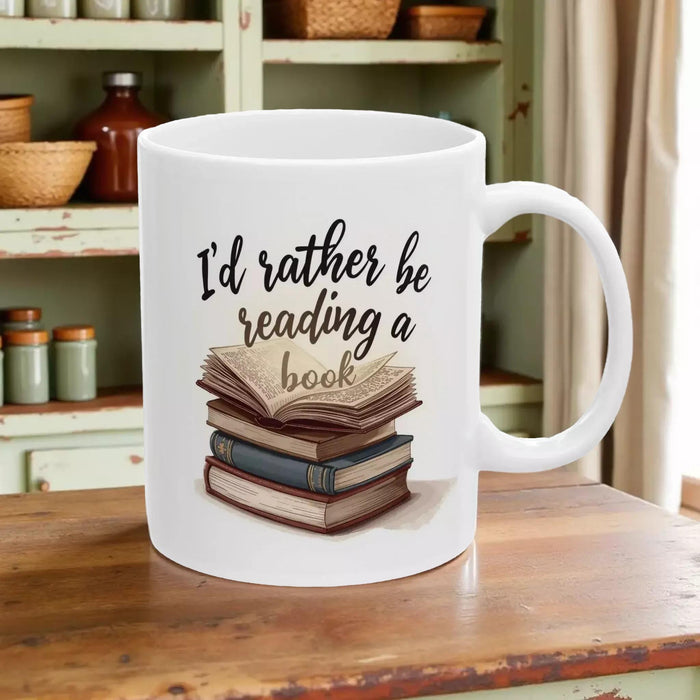 A beige tote bag with a printed design on it, depicting a stack of books. The text on the bag reads "I'd rather be reading a book".