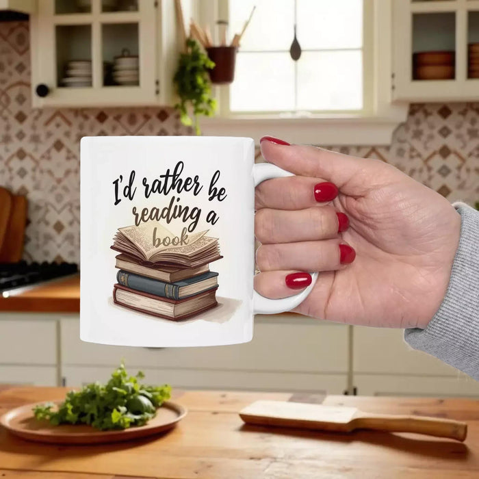 A beige tote bag with a printed design on it, depicting a stack of books. The text on the bag reads "I'd rather be reading a book".