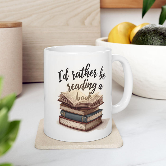 A beige tote bag with a printed design on it, depicting a stack of books. The text on the bag reads "I'd rather be reading a book".