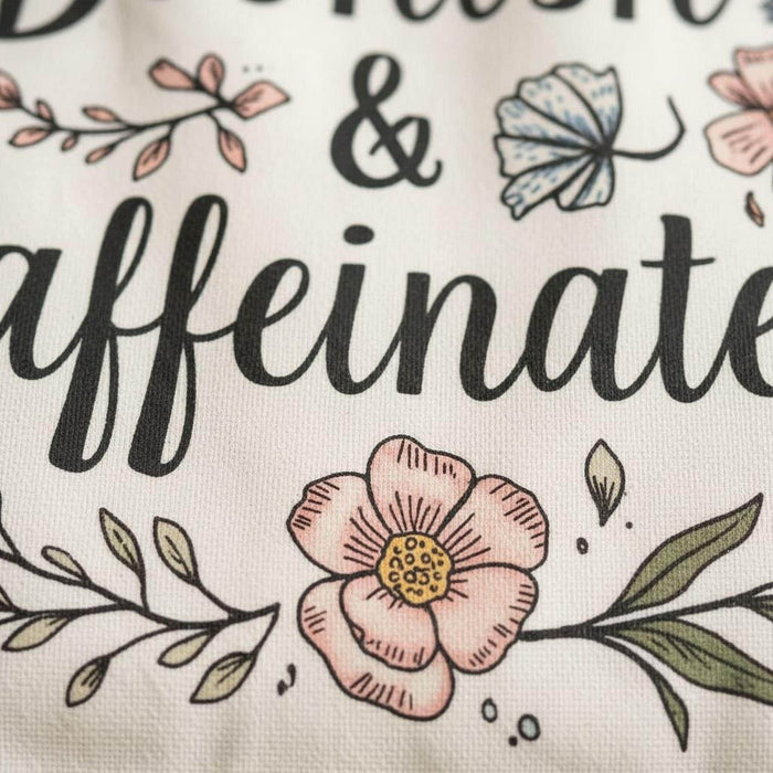 A white tote bag with a floral design and a purple handle, along with a white mug with a floral design and a purple handle, both sitting on a beige surface.
