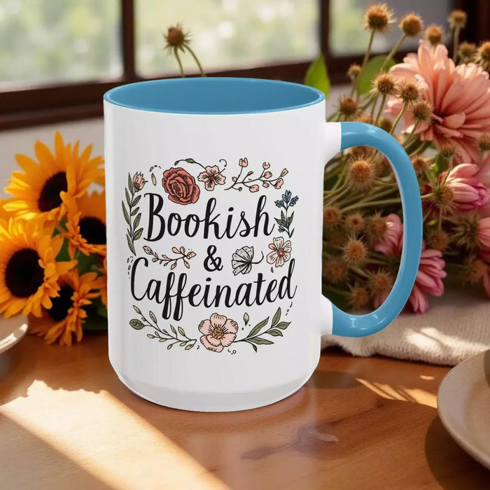 A white tote bag with a floral design and a purple handle, along with a white mug with a floral design and a purple handle, both sitting on a beige surface.